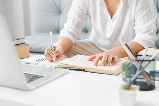 Student writing notes with laptop on desk